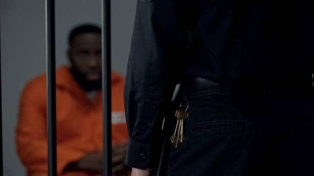 istock Security warden with keys looking at afro-american imprisoned male in cell 1167840135