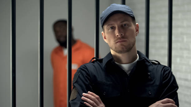 istock Prison warden looking to camera standing near cell with imprisoned afro-american 1167840141