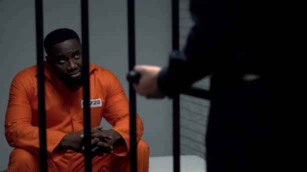 istock Jail guard with baton looking at afro-american prisoner in cell, harassment 1167840173