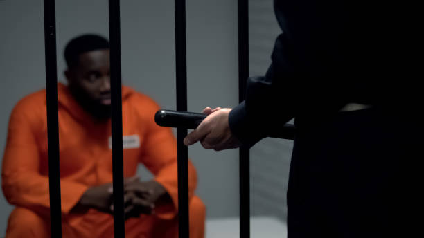 istock Afro-american prisoner in cell looking at jail guard with baton, harassment 1167840184