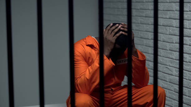 Desperate black prisoner sitting in cell, wrongly accused person, faulty system stock photo