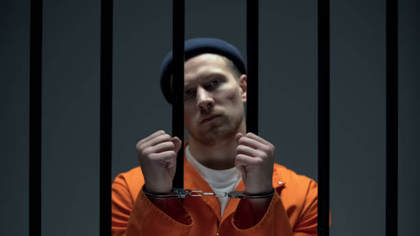 istock Dangerous arrogant prisoner standing behind bars and showing handcuffed hands 1167840333