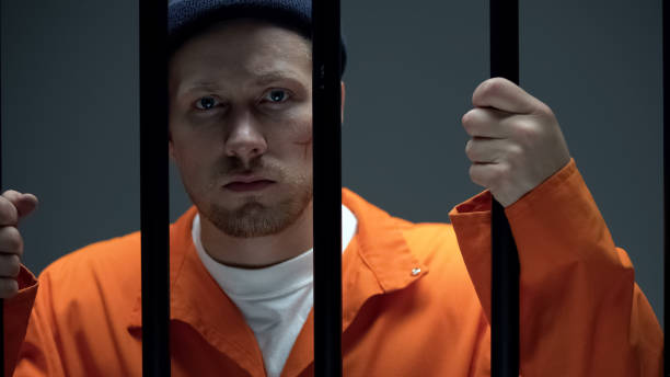 istock Disappointed criminal with scar on face holding prison bar, looking at camera 1167840353