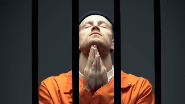 istock Imprisoned man in despair praying behind cell bars, feeling guilty about crime 1167840387