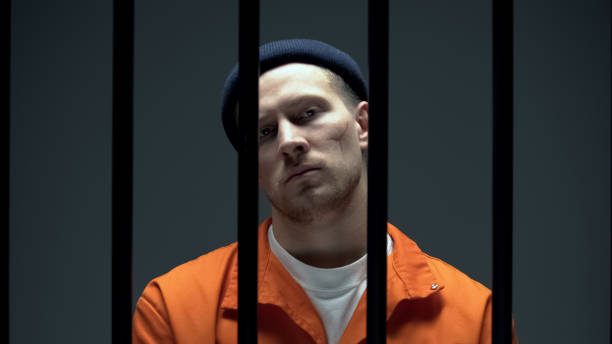 istock Dangerous criminal with scared face looking at camera behind prison bars 1167840399