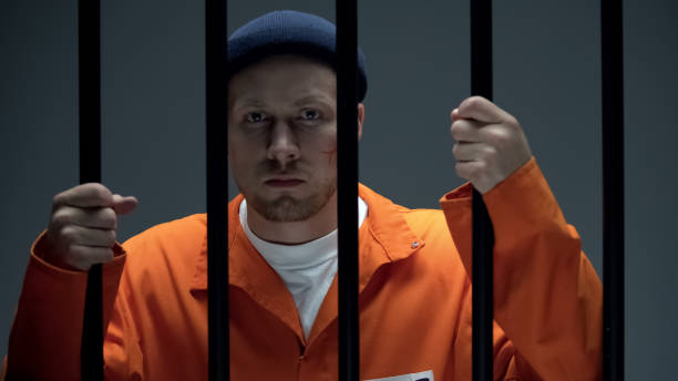 istock Dangerous imprisoned criminal with scar on face holding bars looking at camera 1167840416