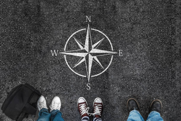 people with a shoes is standing next to compass sign on road asphalt