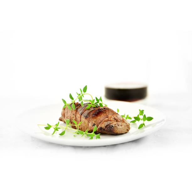 Wild fillet of venison, grilled, carved and served for eating with fresh green thyme garnish, shot against a white background with accommodation for copy space. Displayed text can easily be removed.
