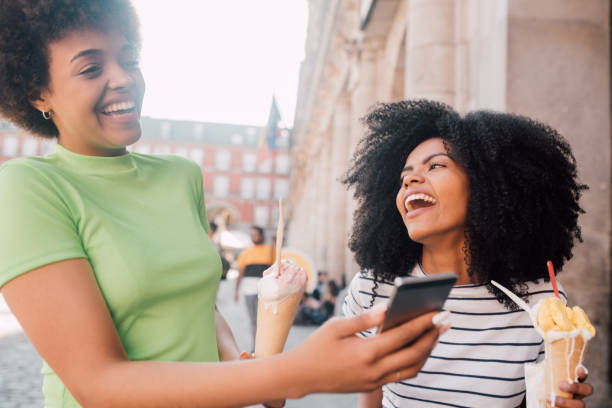 istock Two Girlfriends eating ice cream and using smartphone outdoors 1167849123