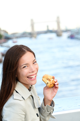 Scones - woman eating scone in London. Happy girl holding British pastry by River Thames, London, England, United Kingdom