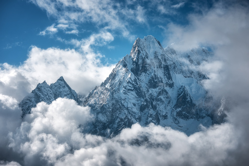 Manaslu mountain with snowy peak in clouds in sunny bright day in Nepal. Landscape with high snow covered rocks and blue cloudy sky. Beautiful nature. Fairy scenery. Aerial view of Himalayan mountains