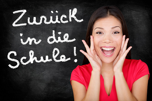 Zuruck in die Schule - German student screaming happy Back to School written in German on blackboard by female teacher. Smiling happy woman teaching German language or university student in college