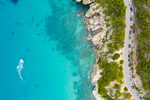 View from above, stunning aerial view of a road that runs along a rocky coast bathed by a turquoise and transparent sea. Cala Gonone, Sardinia, Italy.