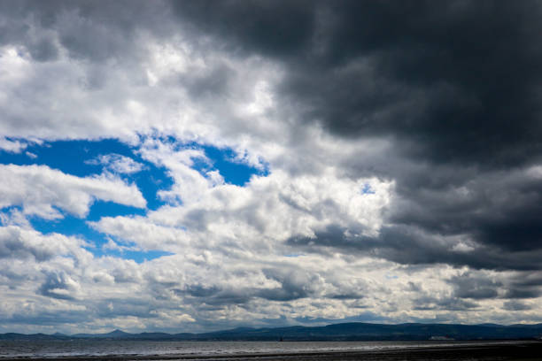 темные грозовые тучи бросают тень на пляж, как перевал над бычьим островом во врем�я отлива с дублинским заливом и дублинскими горами на зад� - overcast republic of ireland cloudscape cloud стоковые фото и изображения