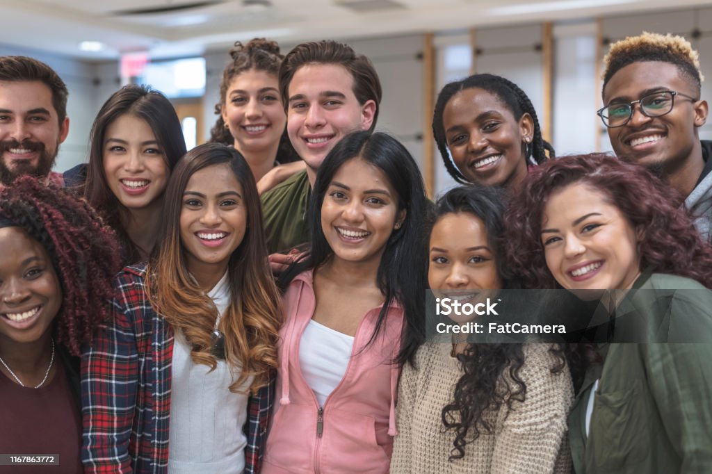 Multi-Ethnic Group of University Students Sitting Inside Together A large-sized group of university-aged students, both male and female, are standing inside the school while relaxing before class. They are dressed in casual but stylish clothing while smiling in this portrait. Equality Stock Photo