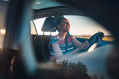 Young African-American woman in a car. She is driving, smiling and looking out. She is singing and having fun on a sunny spring afternoon.