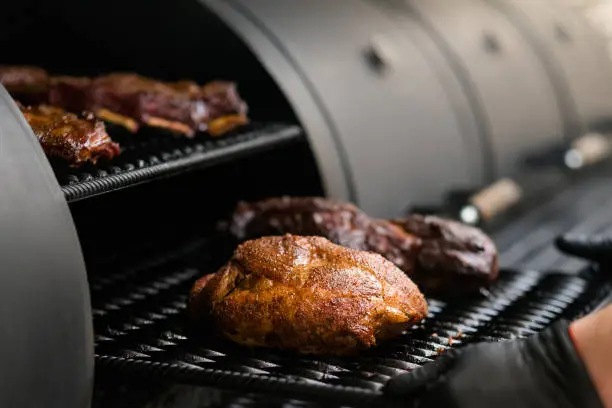 Grill restaurant kitchen. Closeup of chef cooking poultry, beef and pork meat, ribs in BBQ smoker.