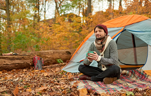 Couple of two attractive backpackers camping in leaves covered woods and warming up with hot chocolate.