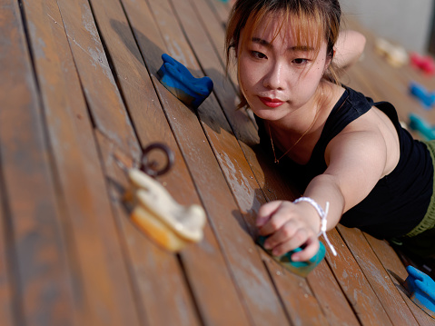 Close up portrait of young Chinese woman practicing rock climbing on a rock wall, sweat at her face.