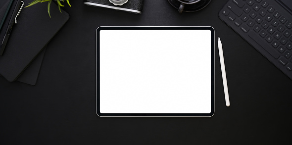 Top view of blank screen tablet on black leather background in dark stylish workplace and office supplies