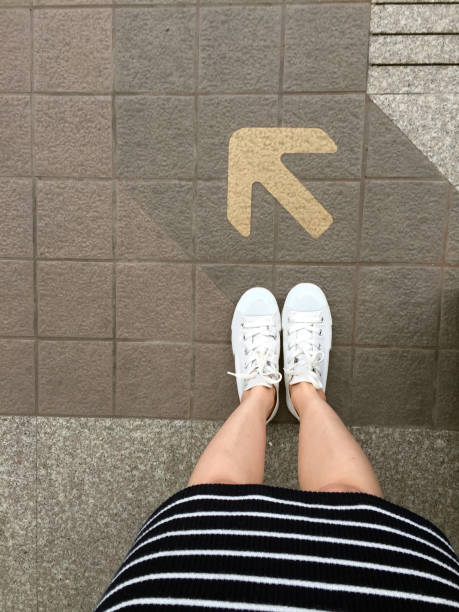 道路上の足と矢。矢印方向の黄色の記号と床に立っています。トップビュー。 - choice teenager footpath arrow sign ストックフォトと画像