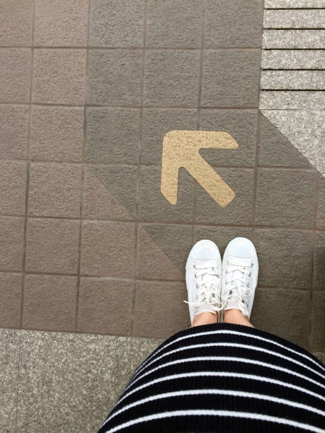 道路上の足と矢。矢印方向の黄色の記号と床に立っています。トップビュー。 - choice teenager footpath arrow sign ストックフォトと画像