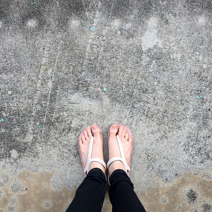 Selfie of feet and legs with shoe on road street, top view. Young woman wearing beige sandals shoes or footwear on concrete floor background. Beauty and fashion concept.