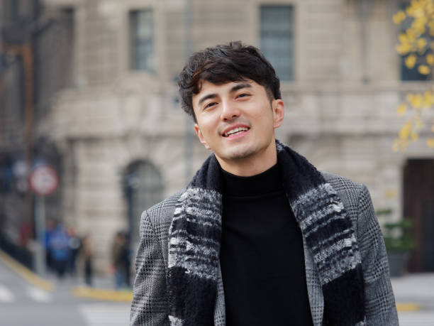 Portrait of a handsome Chinese young man in casual suit smiling and looking at camera confidently with Shanghai bund background, winter fashion, cool young man lifestyle. stock photo