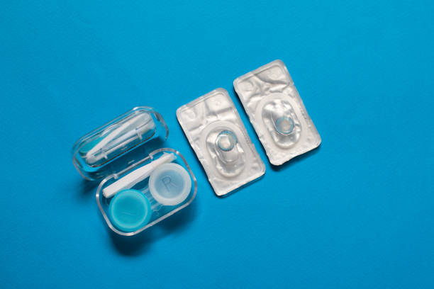 blue color pair of contact lenses in blisters with blue contact lens case and tweezers on blue background - lens contact lens glasses transparent imagens e fotografias de stock