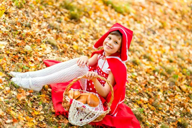 Photo of girl in a red dress sitting on yellow foliage in autumn