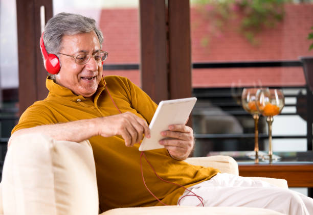 senior man using digital tablet and headphones - ipad senior adult facebook sofa imagens e fotografias de stock