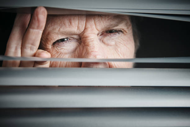 istock Senior woman can't see clearly, looking nervously through blind 1167907996