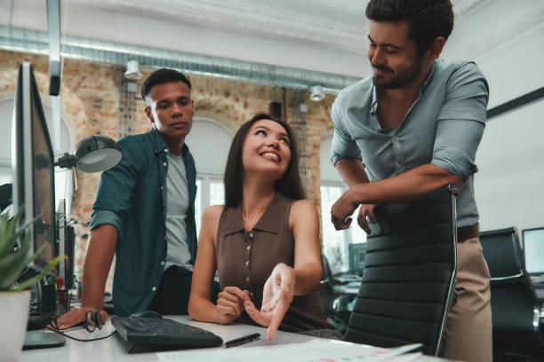 istock Discussing project. Group of young and cheerful three people in casual clothes analyzing data and smiling while working in modern office 1167909217