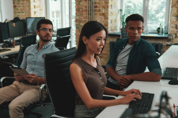 istock Quick meeting. Group of cheerful young employees working on computers and discussing daily tasks while sitting in modern open space 1167909367