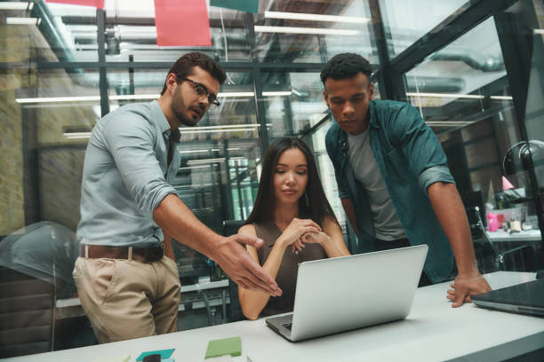 istock Teamwork. Young handsome bearded man pointing at computer monitor and discussing project with his two colleagues while working in modern office 1167910054