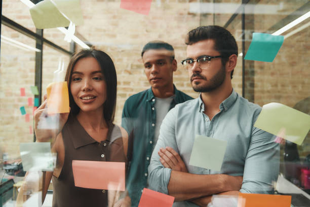 istock Creative ideas. Cheerful male and female colleagues planning working process and using stickers with marker while standing in modern office 1167910077