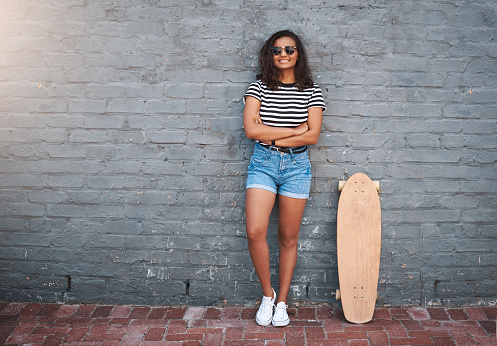 Portrait of a young woman standing with a skateboard against a grey wall