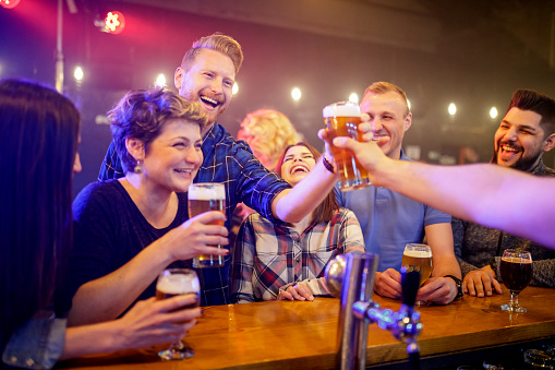 Group of happy people laughing at the bar counter and being served with lager beer