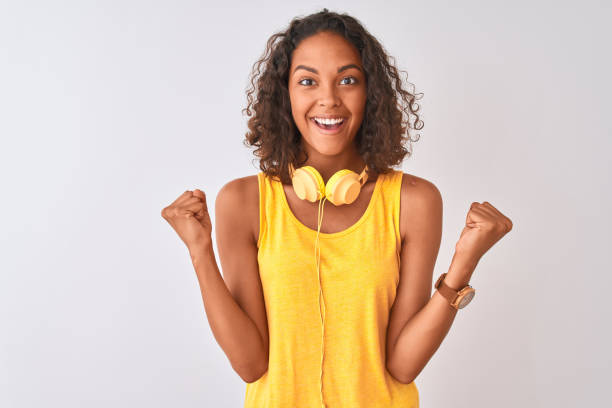 young brazilian woman wearing yellow headphones over isolated white background celebrating surprised and amazed for success with arms raised and open eyes. winner concept. - teenager teenagers only one teenage girl only human face imagens e fotografias de stock