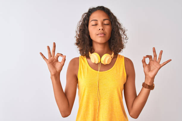 Young brazilian woman wearing yellow headphones over isolated white background relax and smiling with eyes closed doing meditation gesture with fingers. Yoga concept. Young brazilian woman wearing yellow headphones over isolated white background relax and smiling with eyes closed doing meditation gesture with fingers. Yoga concept. teen yoga stock pictures, royalty-free photos & images