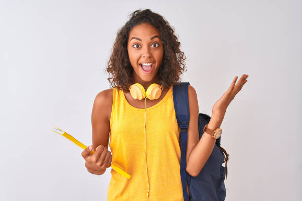 brazilian student woman wearing backpack holding notebook over isolated white background very happy and excited, winner expression celebrating victory screaming with big smile and raised hands - estudante universitária imagens e fotografias de stock