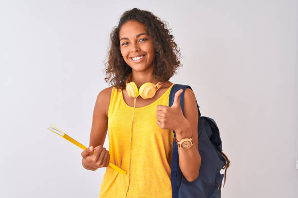 istock Brazilian student woman wearing backpack holding notebook over isolated white background happy with big smile doing ok sign, thumb up with fingers, excellent sign 1167925314
