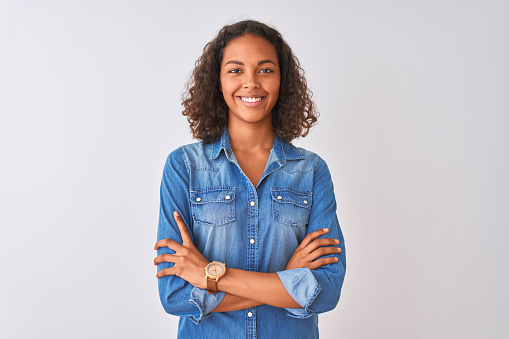 Young brazilian woman wearing denim shirt standing over isolated white background happy face smiling with crossed arms looking at the camera. Positive person.