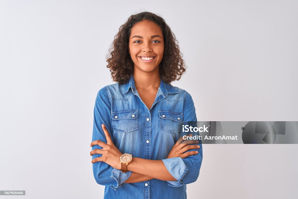 Young brazilian woman wearing denim shirt standing over isolated white background happy face smiling with crossed arms looking at the camera. Positive person. Teenager Stock Photo