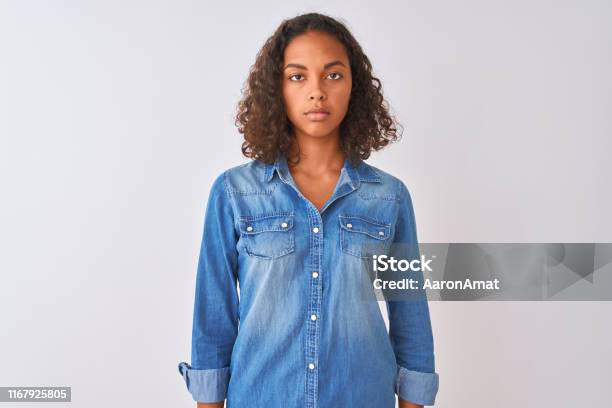 Young Brazilian Woman Wearing Denim Shirt Standing Over Isolated White Background Relaxed With Serious Expression On Face Simple And Natural Looking At The Camera Stock Photo - Download Image Now