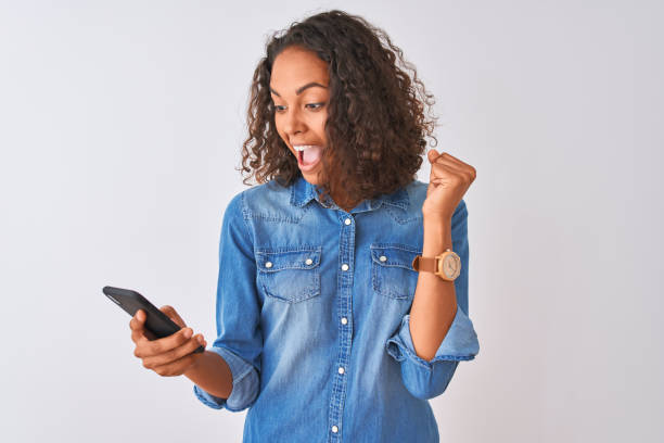 mulher brasileira nova que usa o smartphone que está sobre o fundo branco isolado gritando orgulhoso e comemorando a vitória e o sucesso muito excited, emoção cheering - teenage girls cheerful smiling one person - fotografias e filmes do acervo