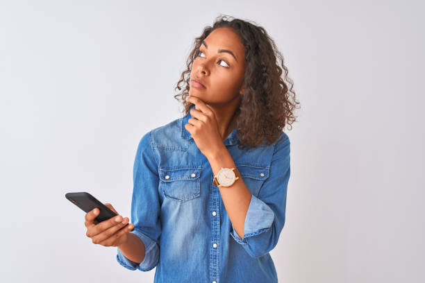 young brazilian woman using smartphone standing over isolated white background serious face thinking about question, very confused idea - teenager teenagers only one teenage girl only human face imagens e fotografias de stock