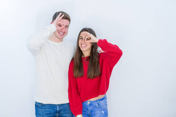 istock Beautiful young couple over white isolated background doing ok gesture with hand smiling, eye looking through fingers with happy face. 1167929574