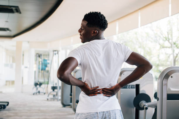 Sportive man touching painful lower back Back view of fit African American man suffering from backache during workout in gym. Sportive man touching painful lower back chronic illness photos stock pictures, royalty-free photos & images
