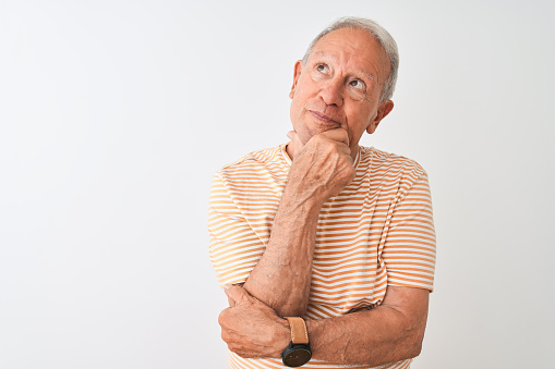 Senior grey-haired man wearing striped t-shirt standing over isolated white background Thinking worried about a question, concerned and nervous with hand on chin